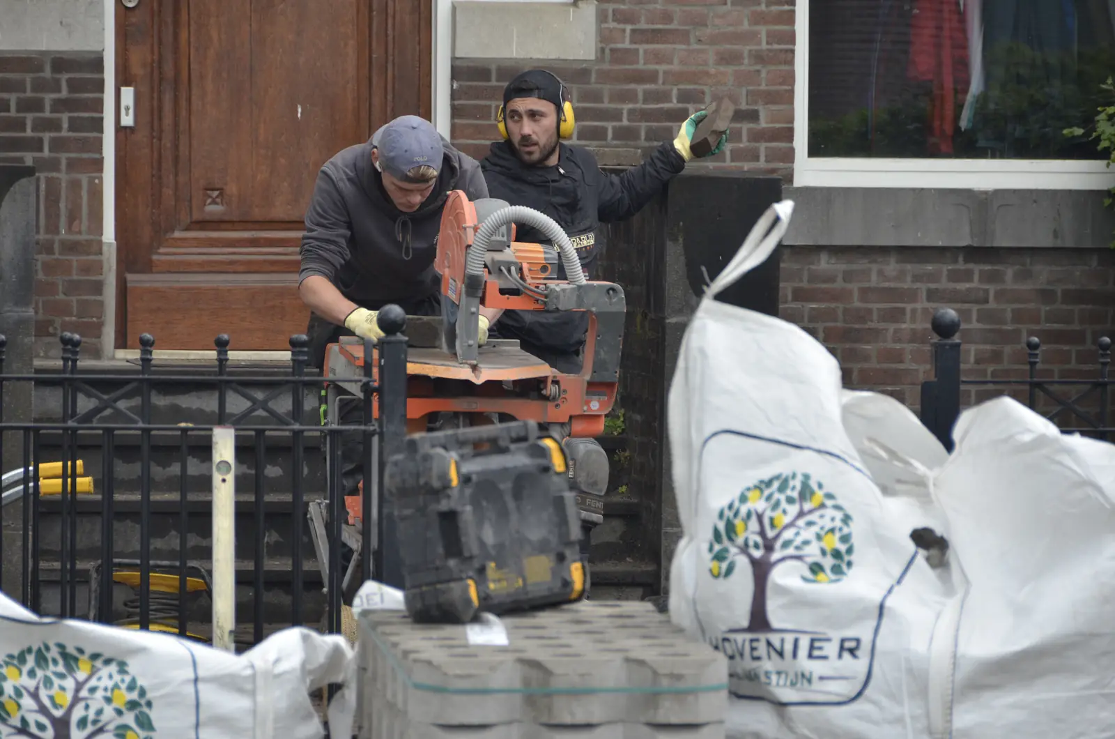 Twee hoveniers zagen stenen op maat, naast big bags met ons logo