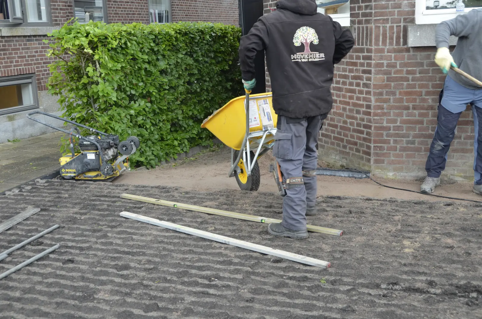 Hovenier met kruiwagen en trilplaat bij de gevel