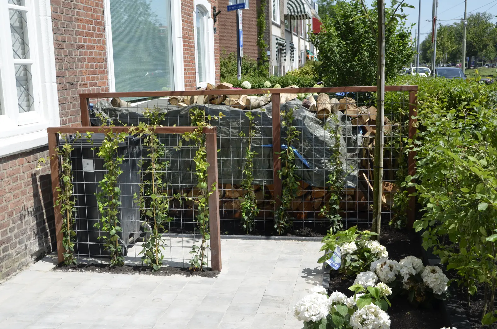 Voortuin met een cortenstalen wand gevuld met haardhout en een klimplantenrek ervoor